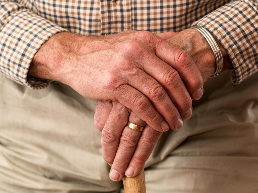 An older man's hands resting on a walking cane